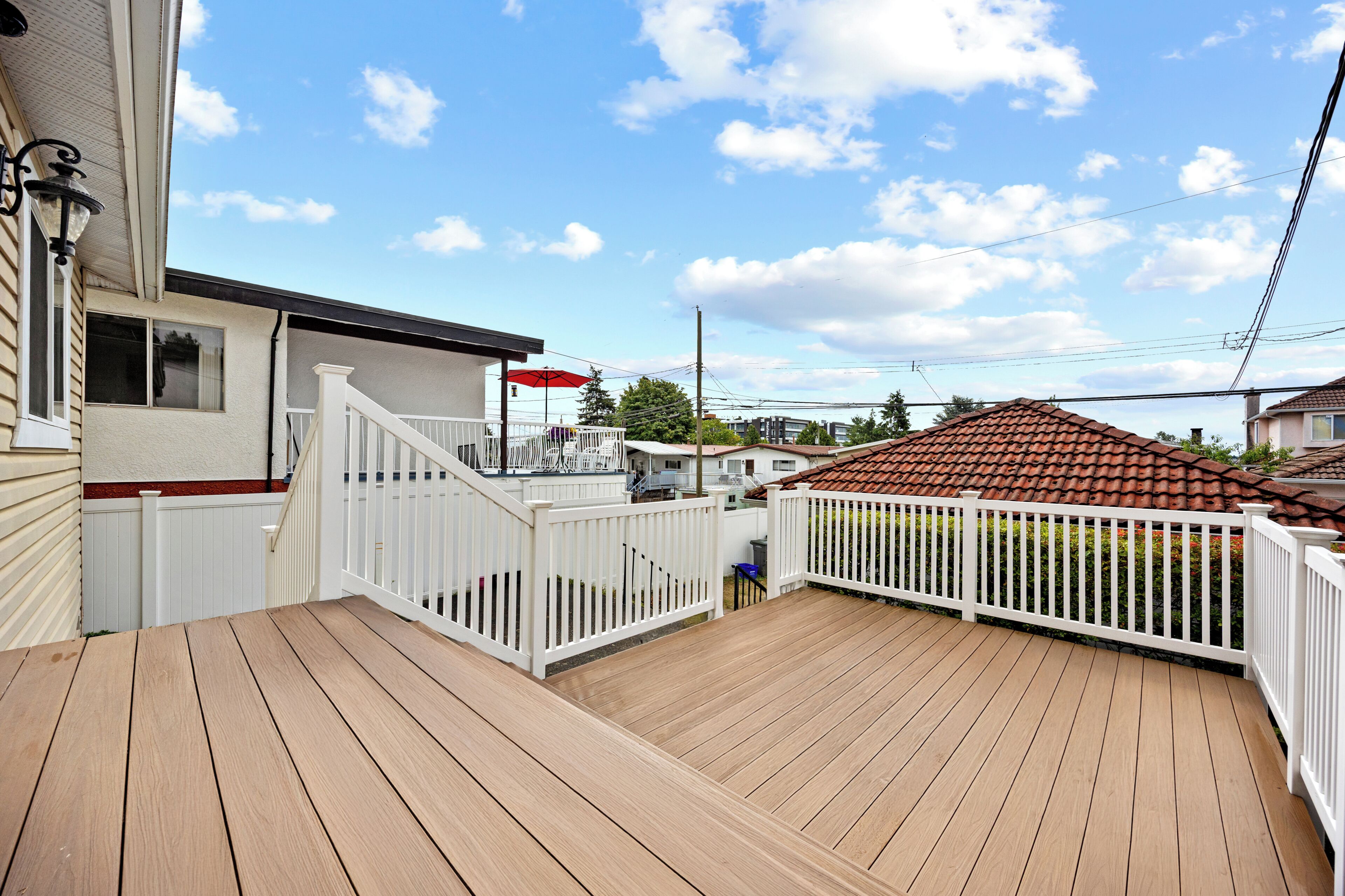 A wooden deck with a white railing, a red umbrella, and a building in the background.