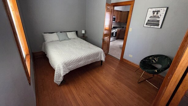 Ein Schlafzimmer mit einem Bett, einem Nachttisch, einem Sessel und einer Tür zum Küchenbereich.