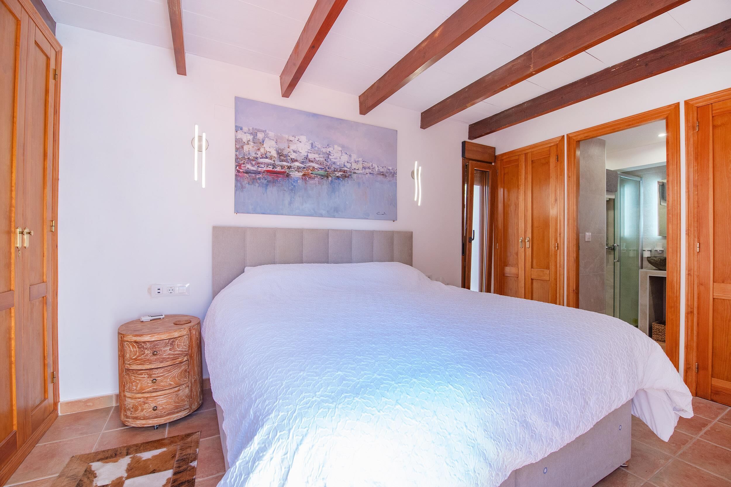 A bedroom with a large bed, wooden wardrobe, and a painting on the wall.
