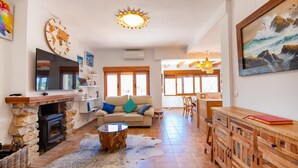 Una sala de estar con chimenea de piedra, televisor, sofá con cojines, una mesa de centro y un mueble de madera.