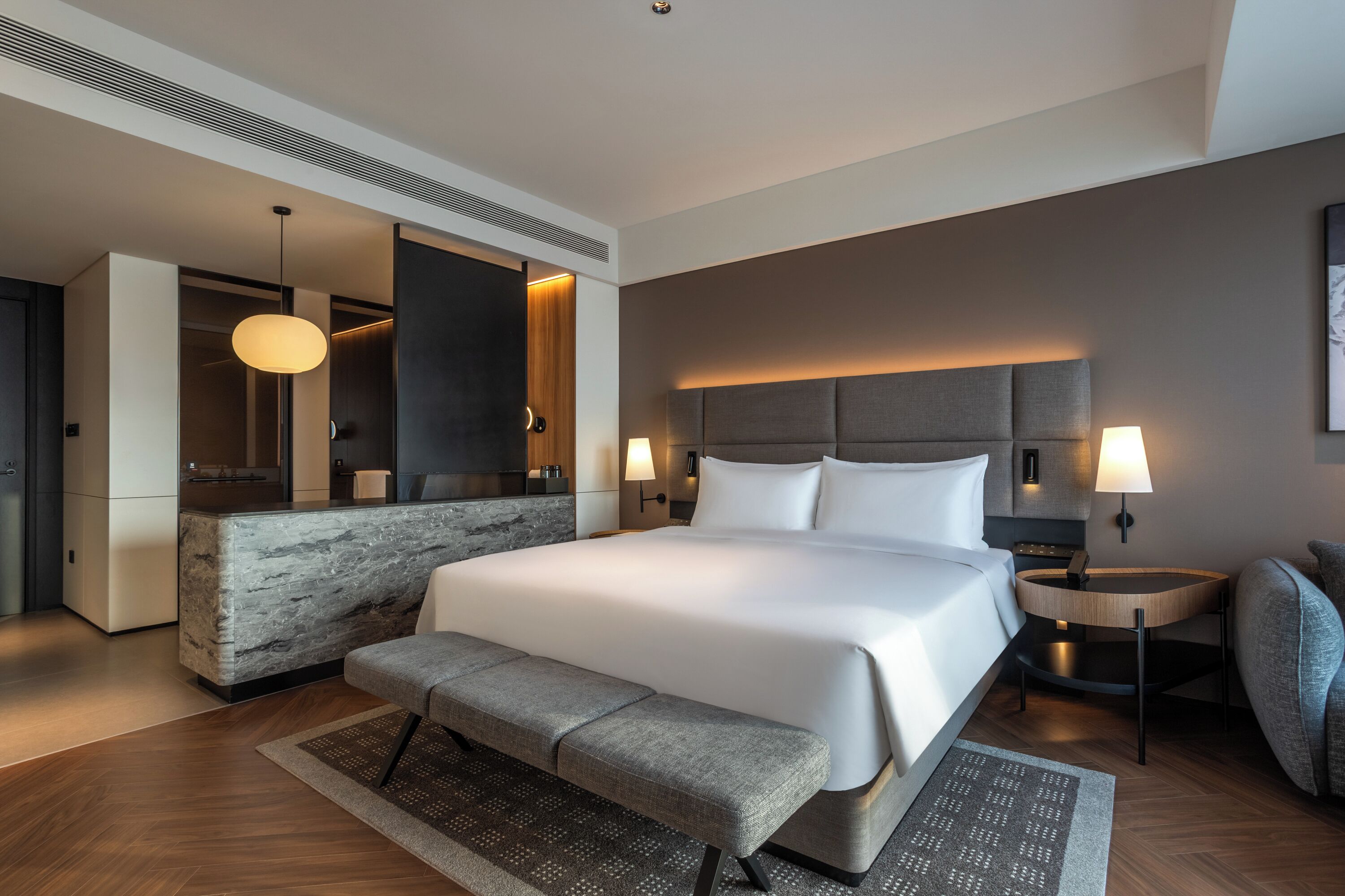 Una habitación de hotel moderna con una cama grande, un banco, un escritorio y un área de estar.