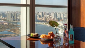 A table with a city view, a bottle, a glass vase with a flower, and pastries. -  IntercityHotel Tianjin Binhai Yujiapu Financial District (Tianjin)