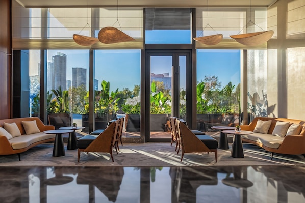 A modern lobby with a glass wall, seating areas, and pendant lighting.
