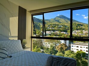 A bedroom with a large window offering a view of a mountainous landscape and a town below.