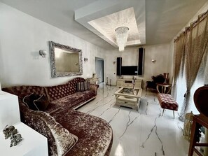 A living room with a sofa, a coffee table, a TV, and a chandelier. - Moonlit Olives - Corfu Luxurious & Stylish Escape (Kokkinogia)