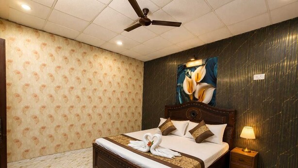 Ein Hotelzimmer mit einem großen Bett, einem Deckenventilator, einem Nachttisch mit Lampe und einer Wand mit floralem Wandpapier.