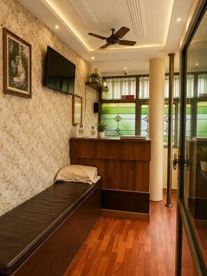 Una habitación con cama, televisor montado en la pared, ventilador de techo y ventana con vitrales.