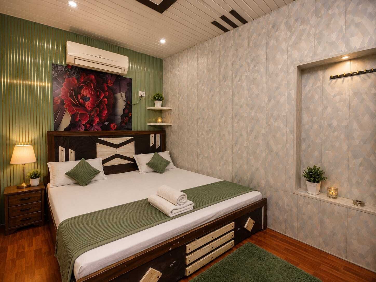 Un dormitorio con cama, mesita de noche, aire acondicionado de pared, un cuadro decorativo y una pequeña estantería con una planta.