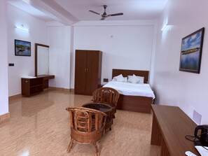 A hotel room with a bed, a wardrobe, a desk, a chair, and a ceiling fan.