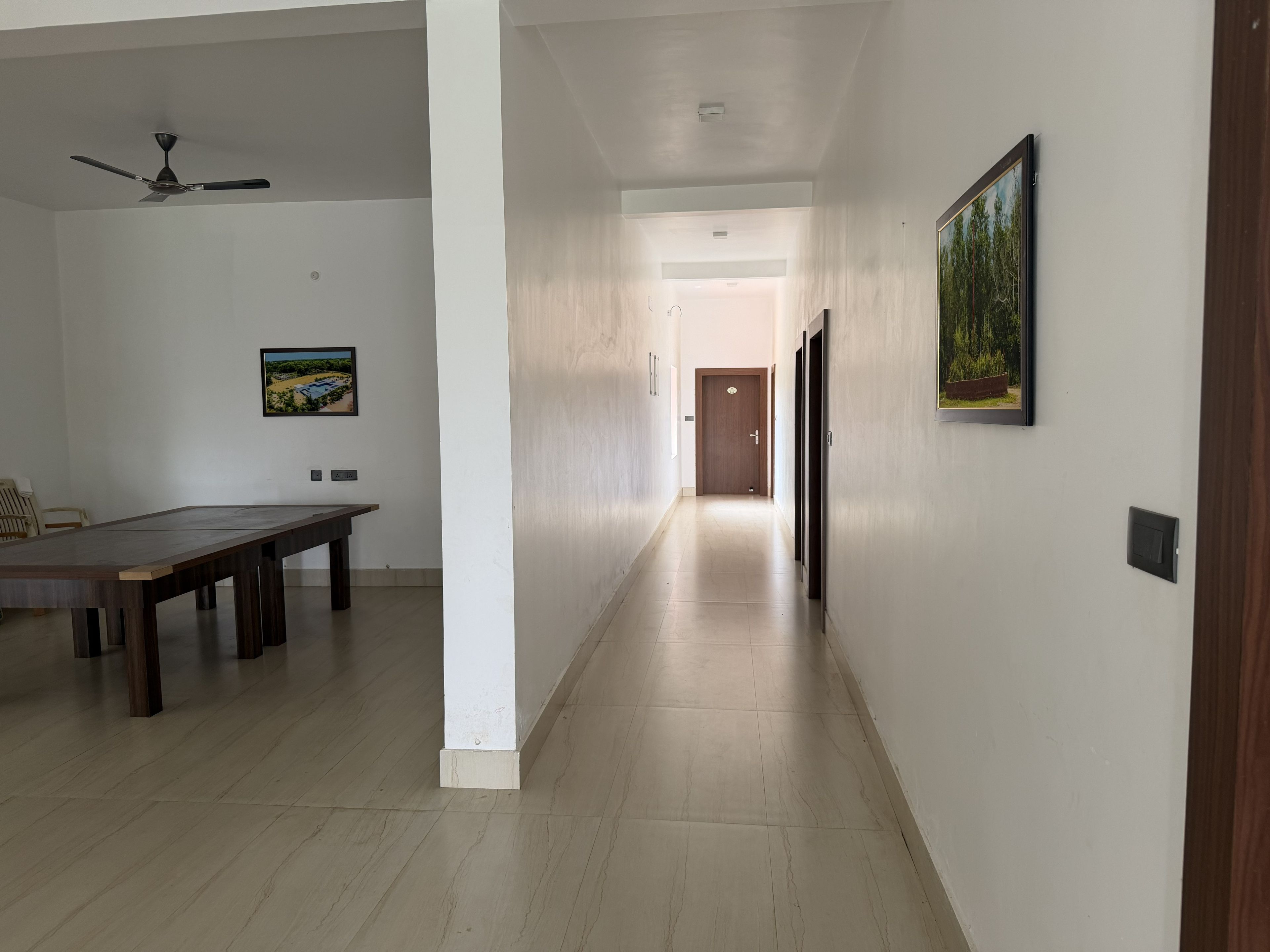 Un pasillo con piso de madera, un ventilador de techo, una mesa de comedor y dos cuadros en las paredes.