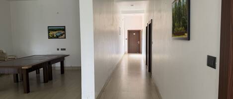 A hallway with a wooden floor, a ceiling fan, a dining table, and two framed pictures on the walls.