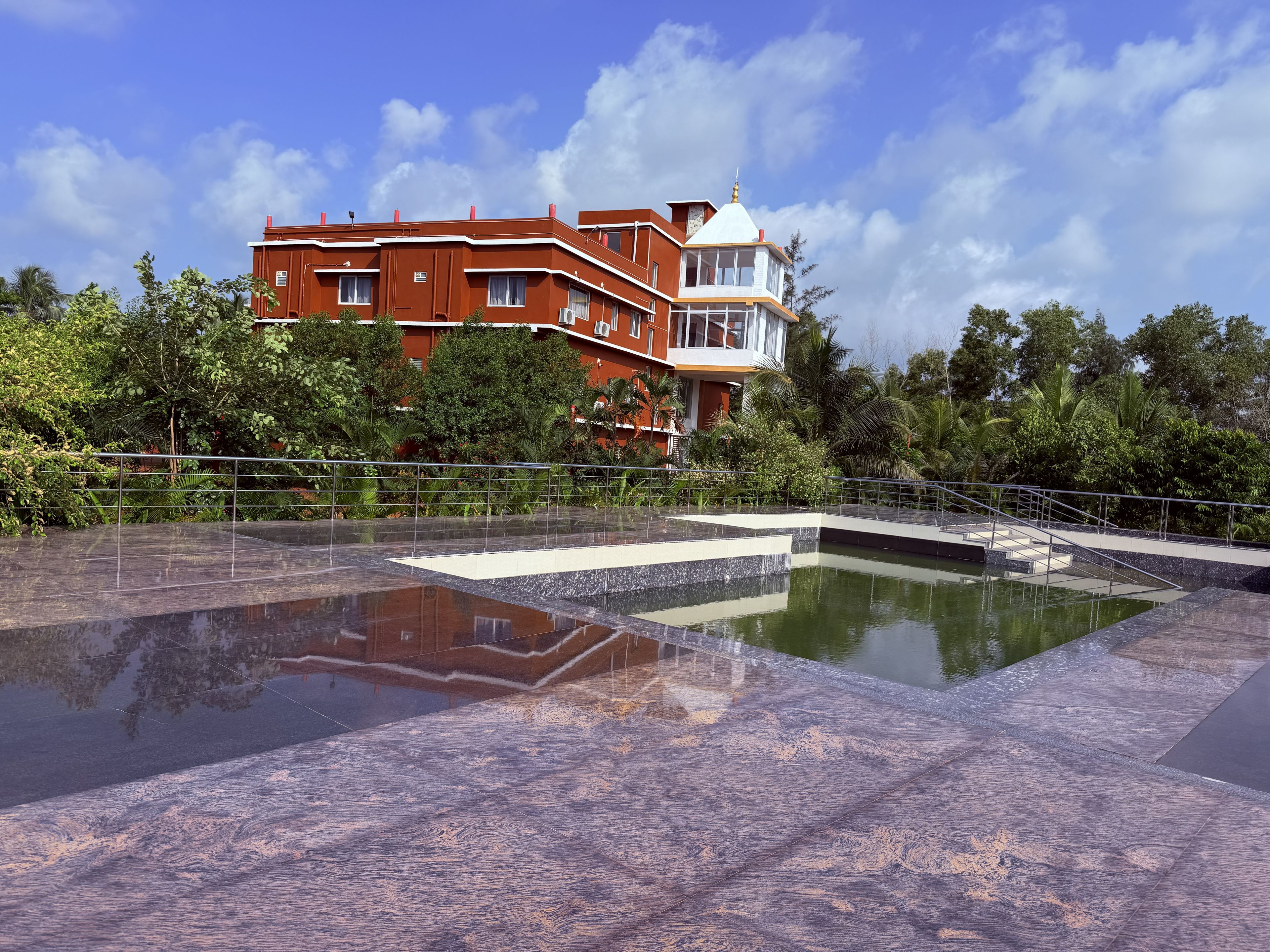 A hotel with a pool, surrounded by greenery and a clear sky.
