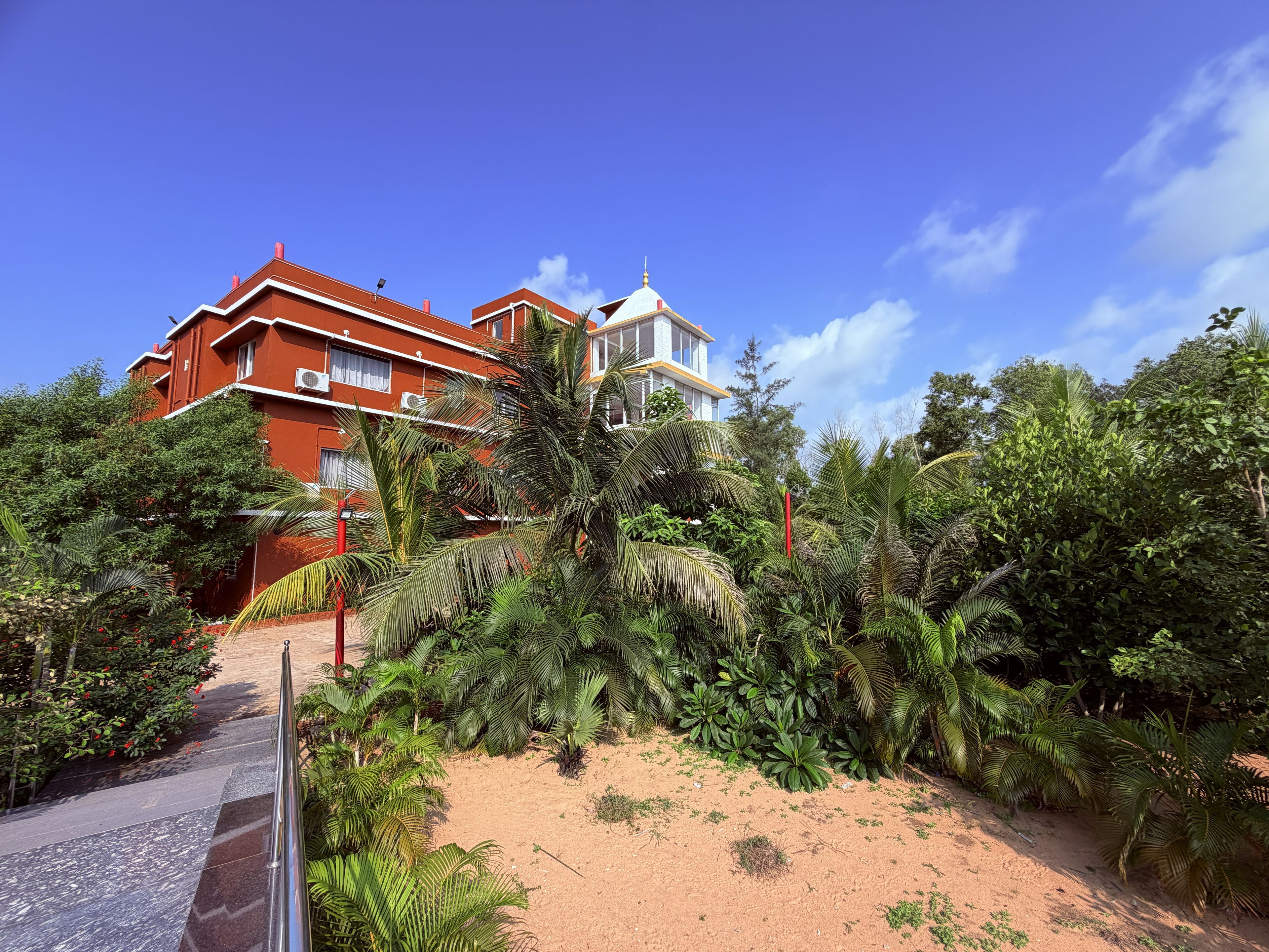 Un edificio de varios pisos con fachada roja, rodeado de exuberante vegetación tropical.