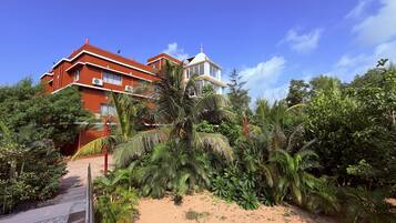 Un edificio de varios pisos con fachada roja, rodeado de exuberante vegetación tropical.