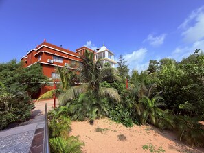 Un edificio de varios pisos con fachada roja, rodeado de exuberante vegetación tropical.