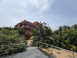 A multi-story building with a red facade, surrounded by dense greenery and a clear sky.