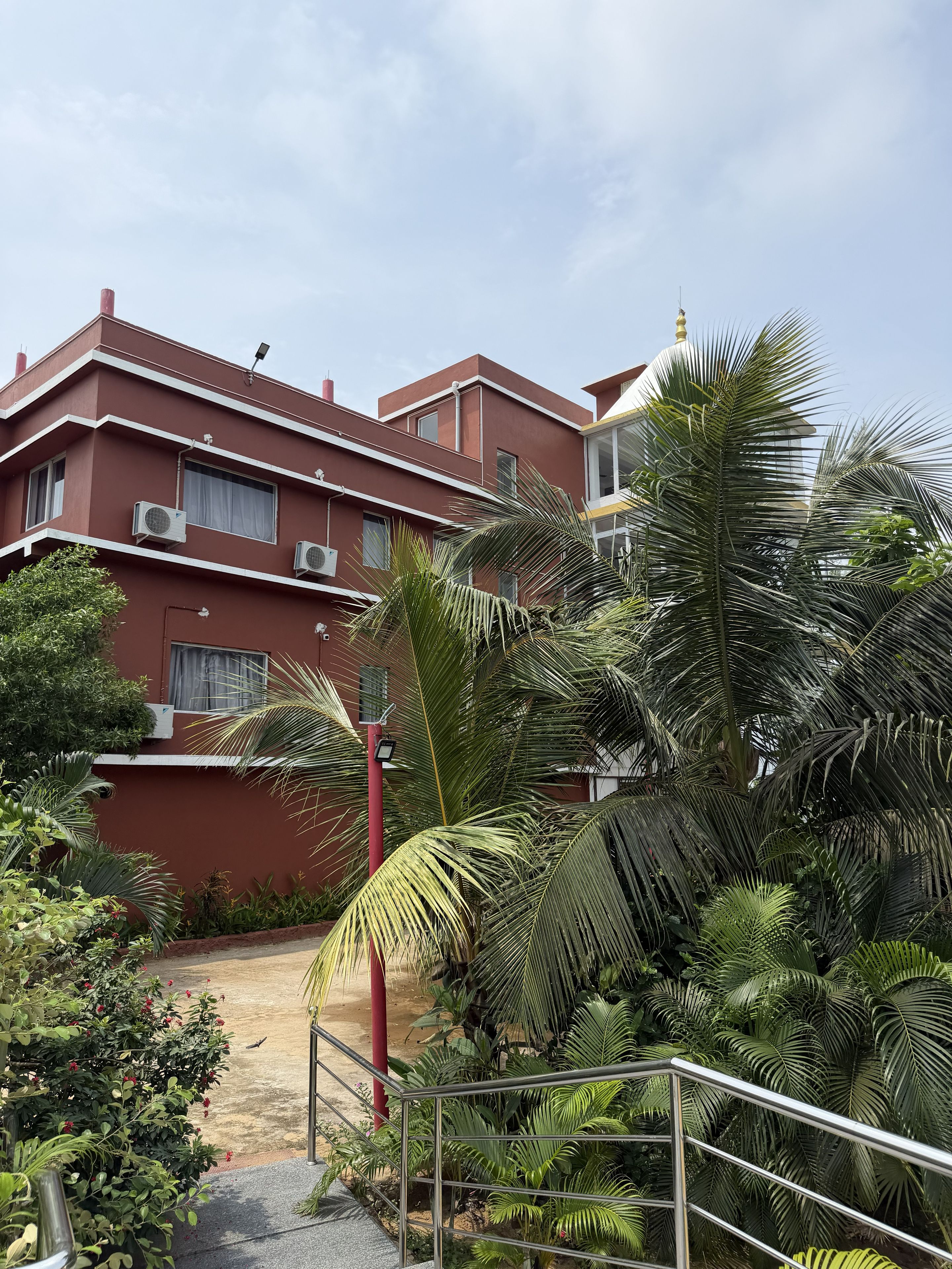 A multi-story building with a red facade, air conditioning units, and a staircase leading to the entrance.