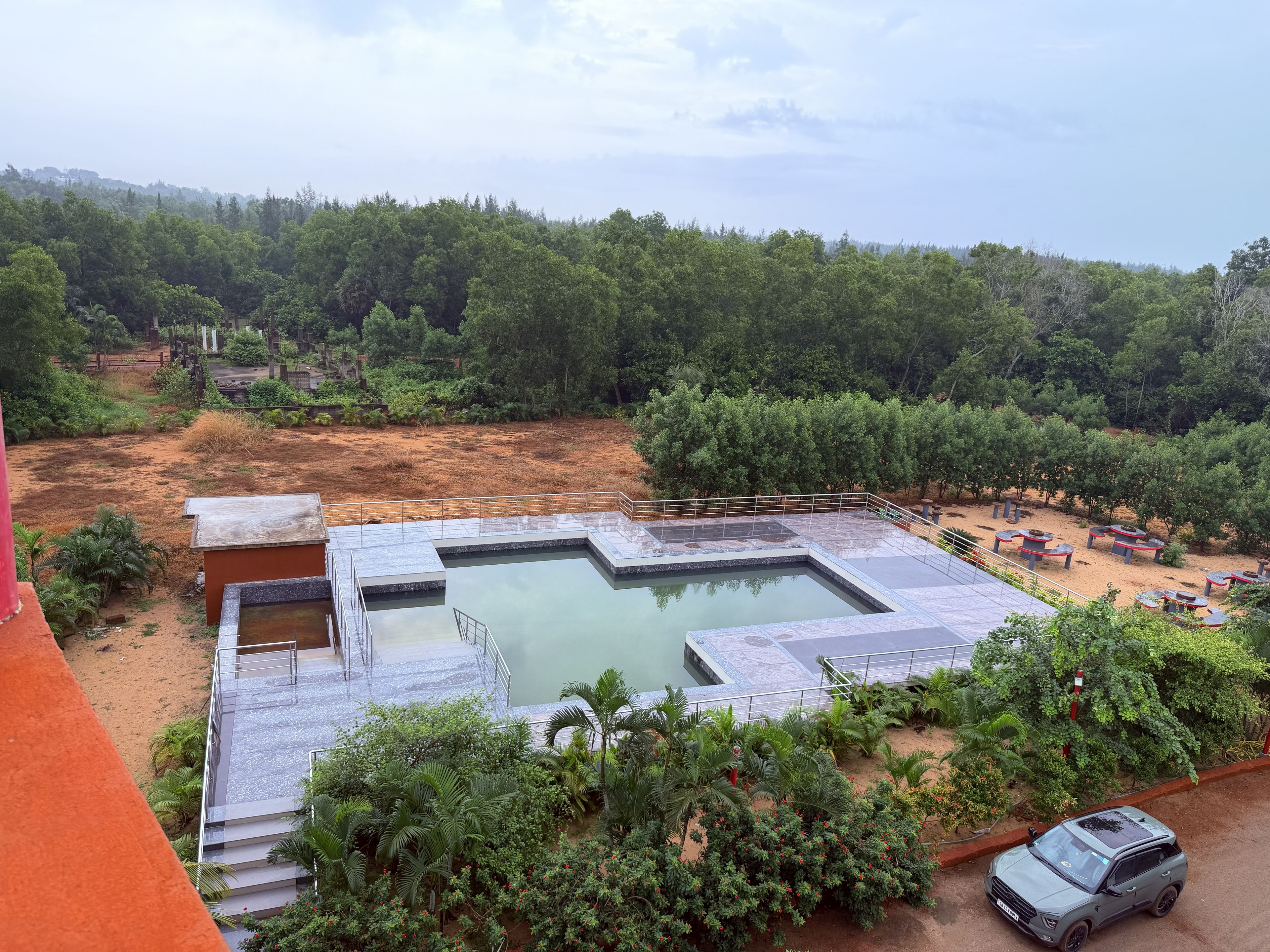 A swimming pool with a surrounding deck, surrounded by dense greenery and trees.