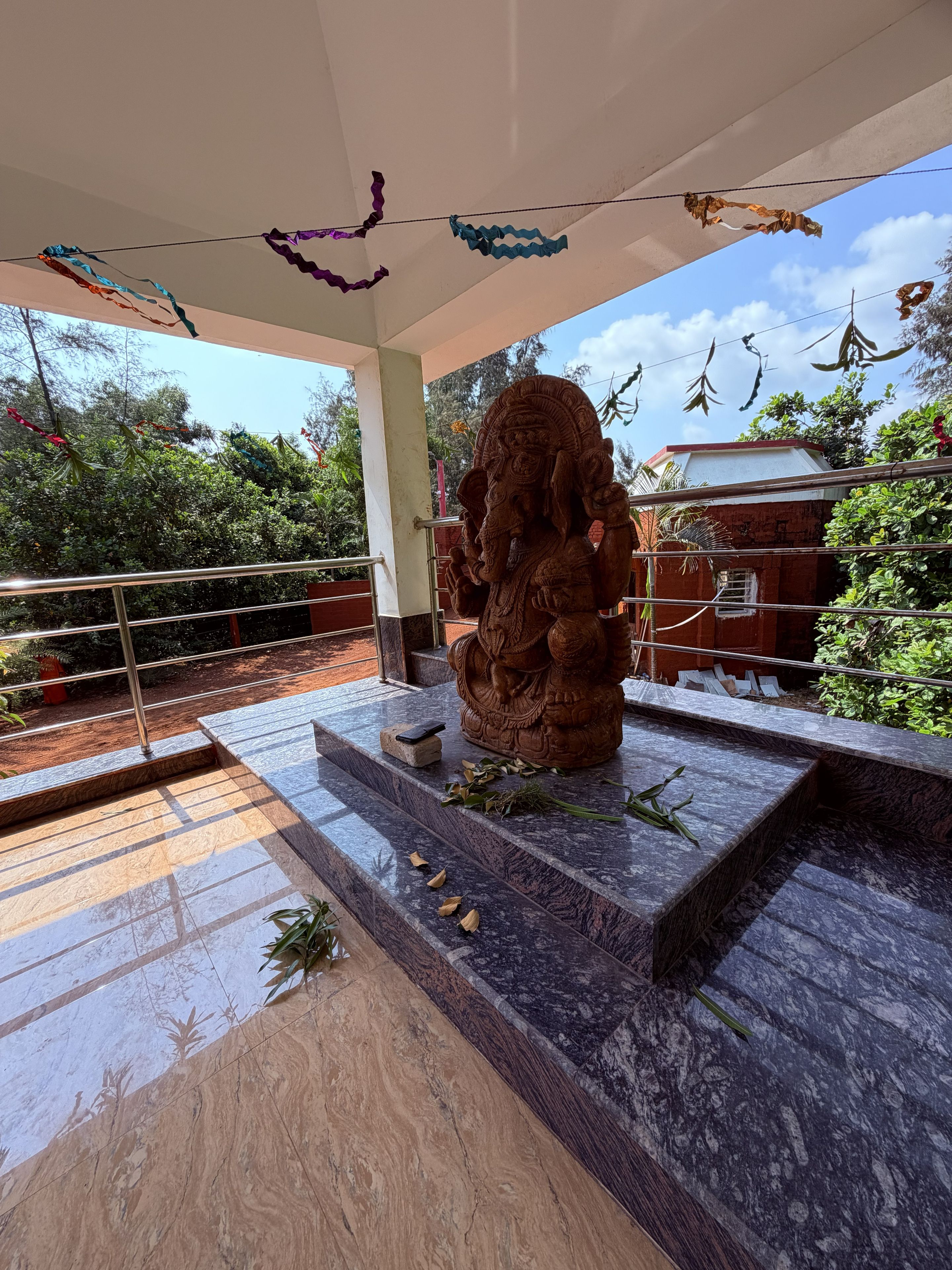 A stone statue of a deity on a marble platform with steps leading up to it, surrounded by greenery and a clear sky.