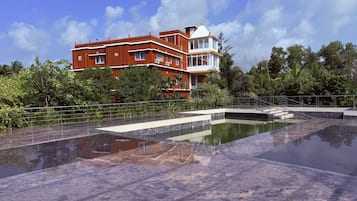 A hotel with a swimming pool, surrounded by lush greenery and a clear blue sky.