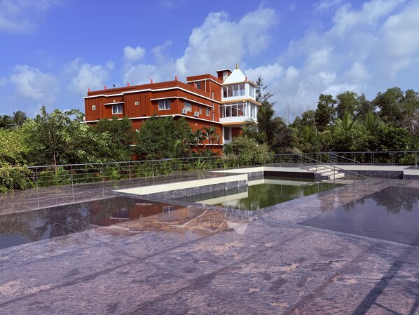 A hotel with a swimming pool, surrounded by lush greenery and a clear blue sky.
