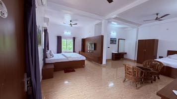A hotel room with a bed, ceiling fans, a TV, a wardrobe, and a seating area with chairs.
