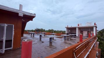 Una terraza en la azotea con varias mesas y sillas, un tanque de agua y un edificio con decoración roja y blanca.