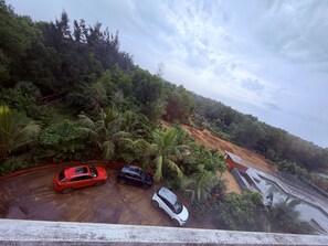 A parking area with three cars, surrounded by dense greenery and a hillside.