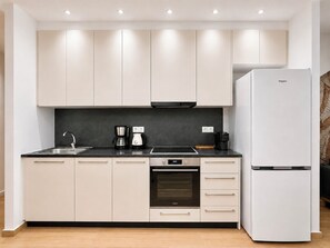 A modern kitchen with white cabinets, a black countertop, a built-in oven, and a white refrigerator. - Galleria The House by ΜΡS (Athina)