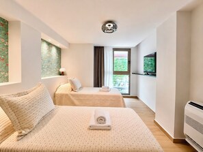 A hotel room with two beds, a television, a window, and an air conditioning unit. - Galleria The House by ΜΡS (Athina)