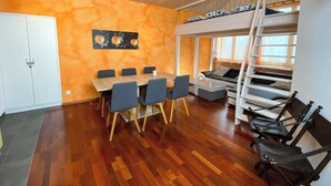 Une pièce avec un plancher en bois, une table à manger avec des chaises, un lit superposé avec une échelle et une armoire blanche.