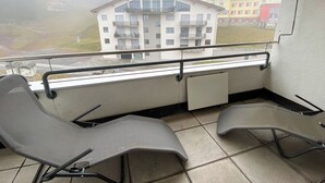Un balcon avec deux chaises, une vue sur des immeubles et une fenêtre.