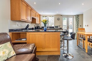 A modern kitchen with wooden cabinets, a marble countertop, and a central island. - Romantic North Wales Meadow Cottage (Ruthin)
