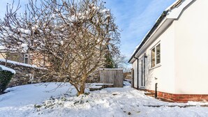 A snow-covered garden with a brick wall, a wooden fence, and a white building with windows. - Romantic North Wales Meadow Cottage (Ruthin)
