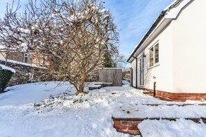A snow-covered garden with a brick wall, a wooden fence, and a white building with windows. - Romantic North Wales Meadow Cottage (Ruthin)