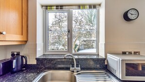 A kitchen with a stainless steel sink, a microwave, and a window with a view of trees. - Romantic North Wales Meadow Cottage (Ruthin)