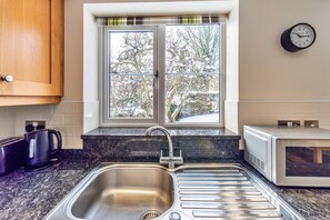 A kitchen with a stainless steel sink, a microwave, and a window with a view of trees. - Romantic North Wales Meadow Cottage (Ruthin)