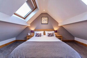 A bedroom with a sloped ceiling, a skylight, a bed with pillows, bedside tables, and a framed picture on the wall. - Romantic North Wales Meadow Cottage (Ruthin)