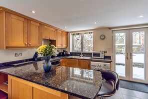 A modern kitchen with wooden cabinets, granite countertops, a built-in oven, and a window with a view of the outside. - Romantic North Wales Meadow Cottage (Ruthin)