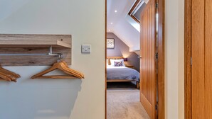 A hallway leading to a bedroom with a sloped ceiling, wooden wardrobe, and a bed with a patterned pillow. - Romantic North Wales Meadow Cottage (Ruthin)