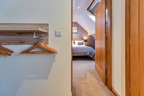 A hallway leading to a bedroom with a sloped ceiling, wooden wardrobe, and a bed with a patterned pillow. - Romantic North Wales Meadow Cottage (Ruthin)