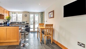 A modern kitchen with a central island, bar stools, and a dining area with a wooden table and chairs. - Romantic North Wales Meadow Cottage (Ruthin)