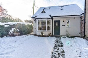 A white cottage with a green door, a bay window, and a small garden area. - Romantic North Wales Meadow Cottage (Ruthin)