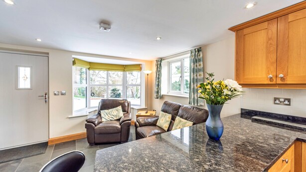 A modern kitchen with granite countertops, a dining area with leather chairs, and a view of the outdoors. - Romantic North Wales Meadow Cottage (Ruthin)