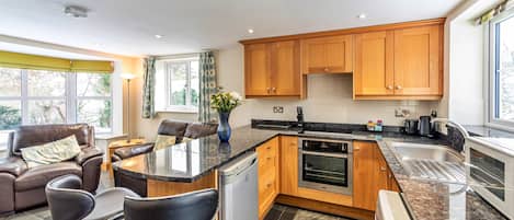 A modern kitchen with wooden cabinets, a built-in oven, and a bar area with stools.