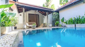 A swimming pool with a covered seating area, surrounded by potted plants and a small outdoor kitchen.