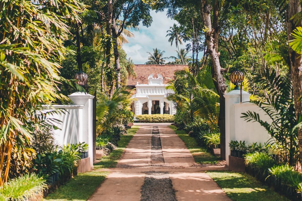 A pathway leading to a building with a white facade and columns, surrounded by lush greenery.