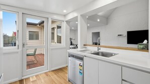 A modern kitchen with a dishwasher, double sink, and a TV mounted on the wall. - South Hobart Designer Retreat (South Hobart)