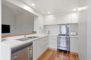 Une cuisine moderne avec des meubles blancs, un évier en acier inoxydable, un lave-vaisselle, une cuisinière et un grille-pain.