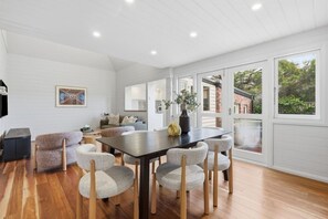 A modern dining area with a wooden table and chairs, a sofa, and a large window with a view of the outdoors. - South Hobart Designer Retreat (South Hobart)